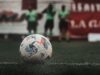 Balón de fútbol sobre el césped con jugadores desenfocados al fondo