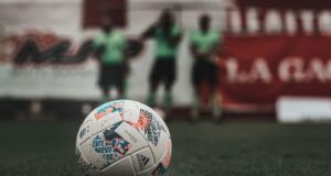 Balón de fútbol sobre el césped con jugadores desenfocados al fondo