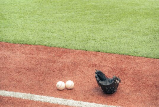 Guante y dos pelotas sobre un terreno de béisbol; fotografía de archivo de 2023.