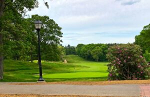 Campo de golf Bethpage Green con bandera, árboles y un sendero en primer plano; fotografía de archivo.