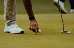 Mano de un golfista colocando una bola junto al putter sobre el green