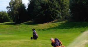Golfista ejecuta un golpe desde un bunker de arena junto al green.