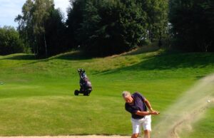 Golfista ejecuta un golpe desde un bunker de arena junto al green.