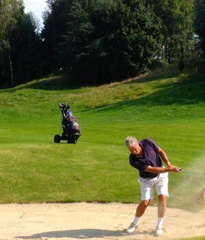 Golfista ejecuta un golpe desde un bunker de arena junto al green.